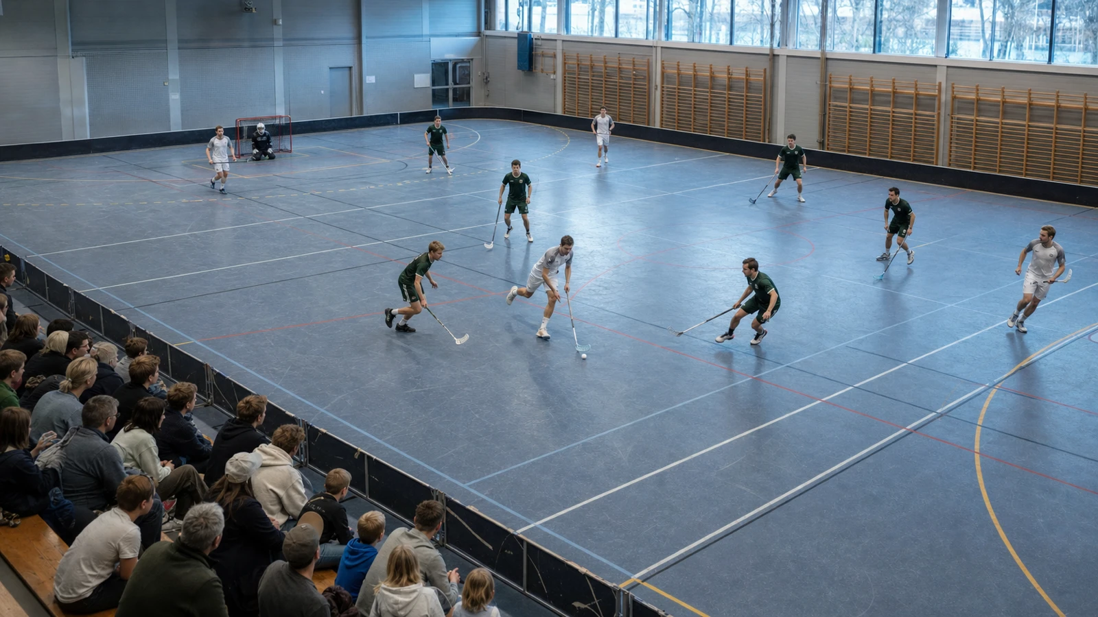Spelare utspridda över en fullstor plan i öppet spel, sett snett uppifrån med publik på bänkläktaren i förgrunden